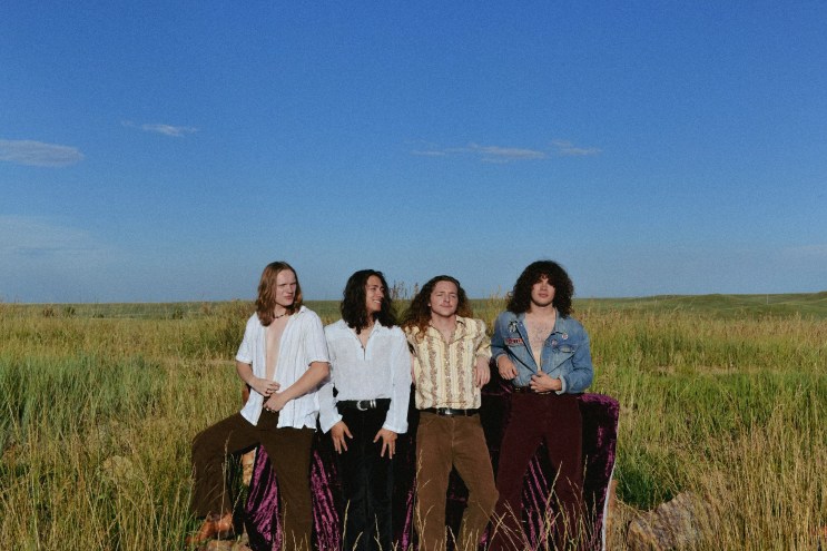 four men standing in a field under blue skies