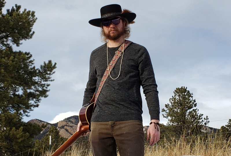Andrew Baker standing outside with guitar strapped around chest and shoulder.