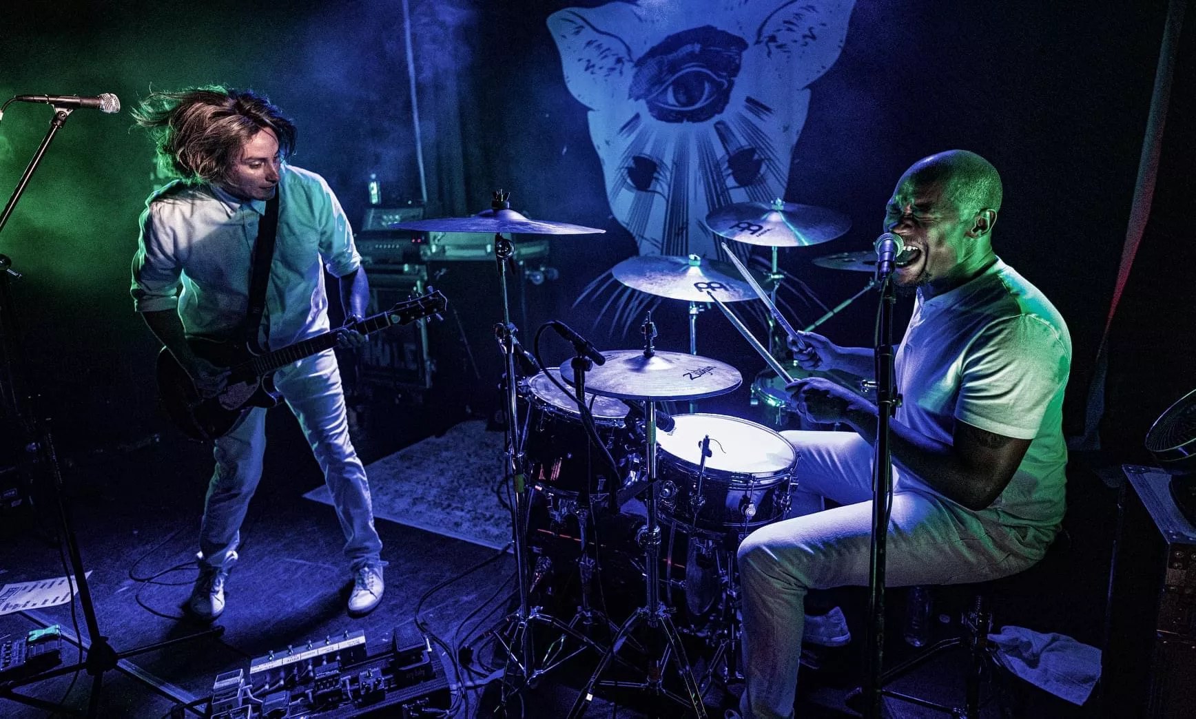 man on stage playing guitar and man playing drums