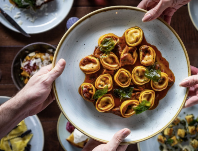 hands passing a dish of pasta