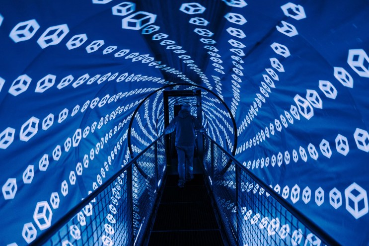 blue lights cover a tunnel-shaped room with a bridge in the center