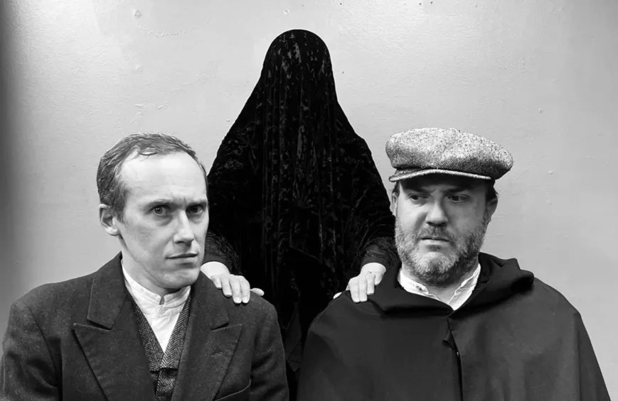a black and white photo of two men in old-fashioned clothing with a figure covered in a black drape behind them