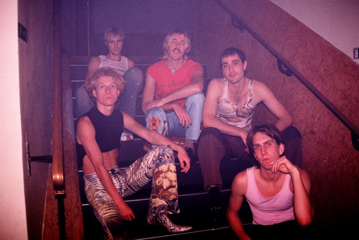 a photograph of five men sitting in stairwell with pink lighting