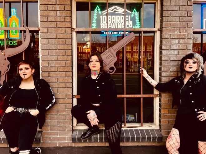 three women standing outside of a brick building with big windows