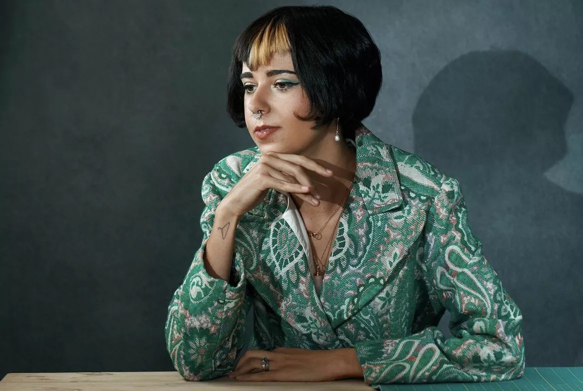 woman and blue suit poses with her head resting on her chin