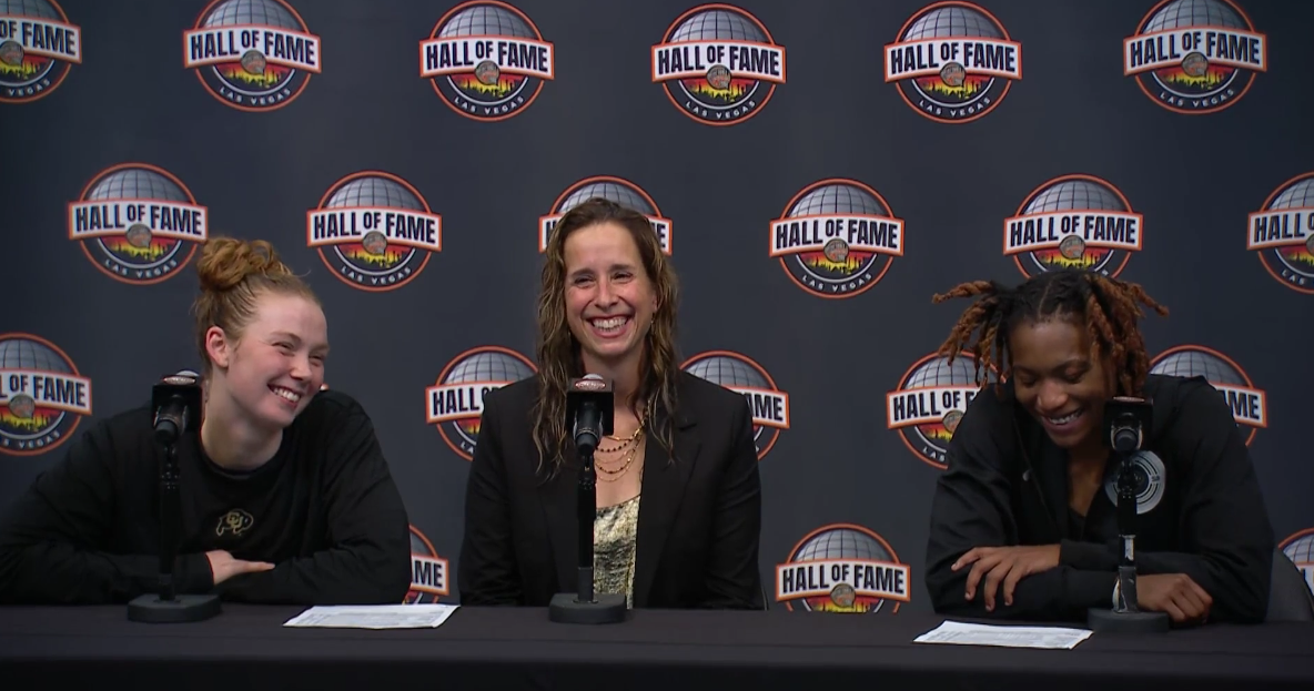 Three women dressed in black sit at a table behind microphones.