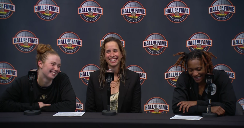 Three women dressed in black sit at a table behind microphones.