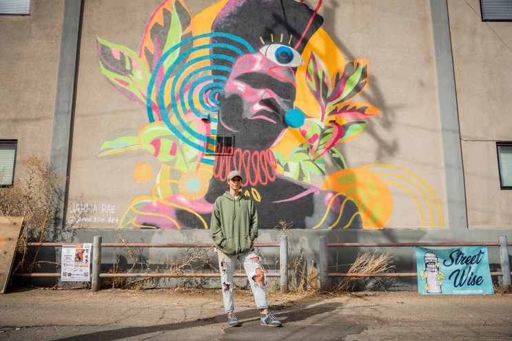 person standing in front of colorful mural outside