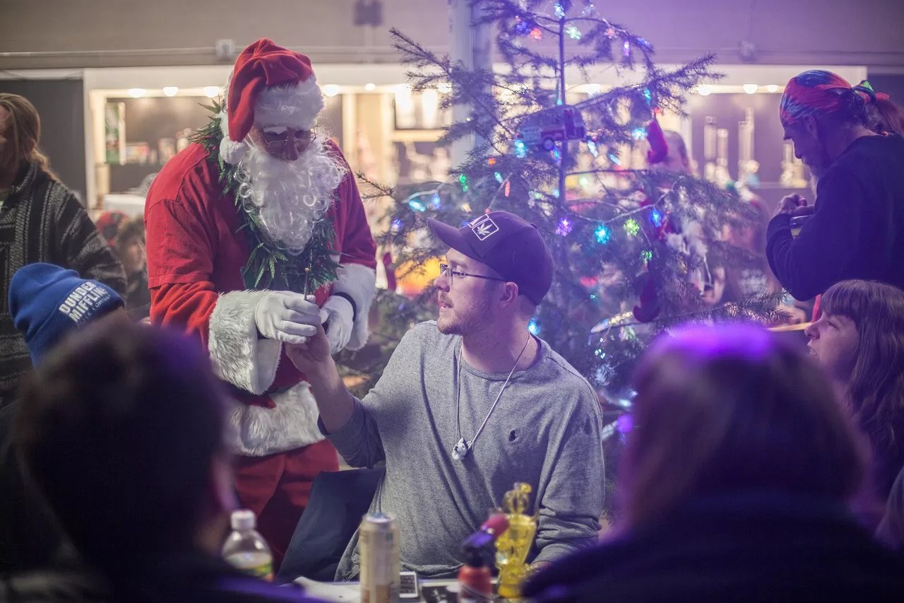 Santa Clause gifting marijuana in front of a Christmas tree