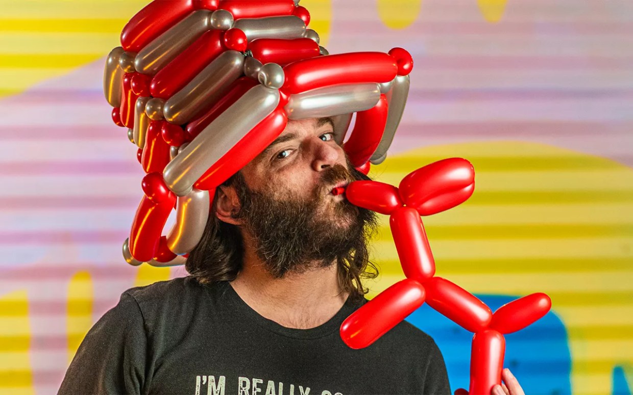 A man kisses a red balloon dog.