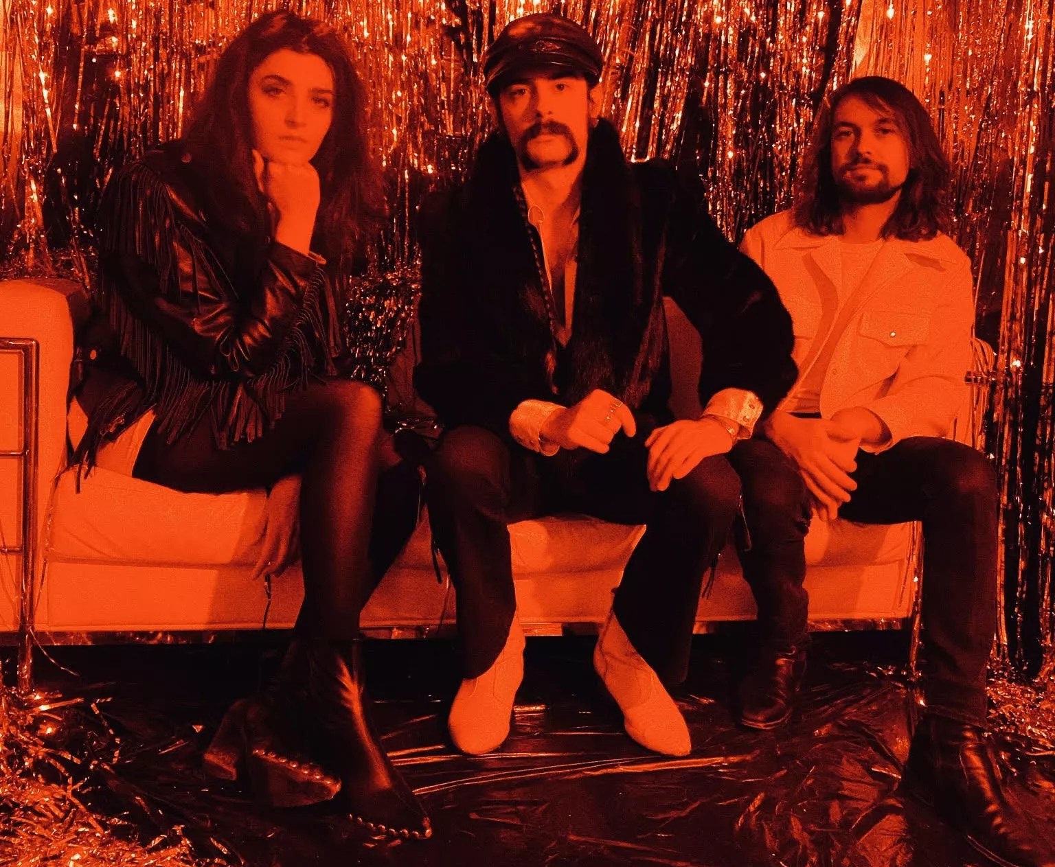 three people sitting on a couch in front of a tinsel wall in orange lighting