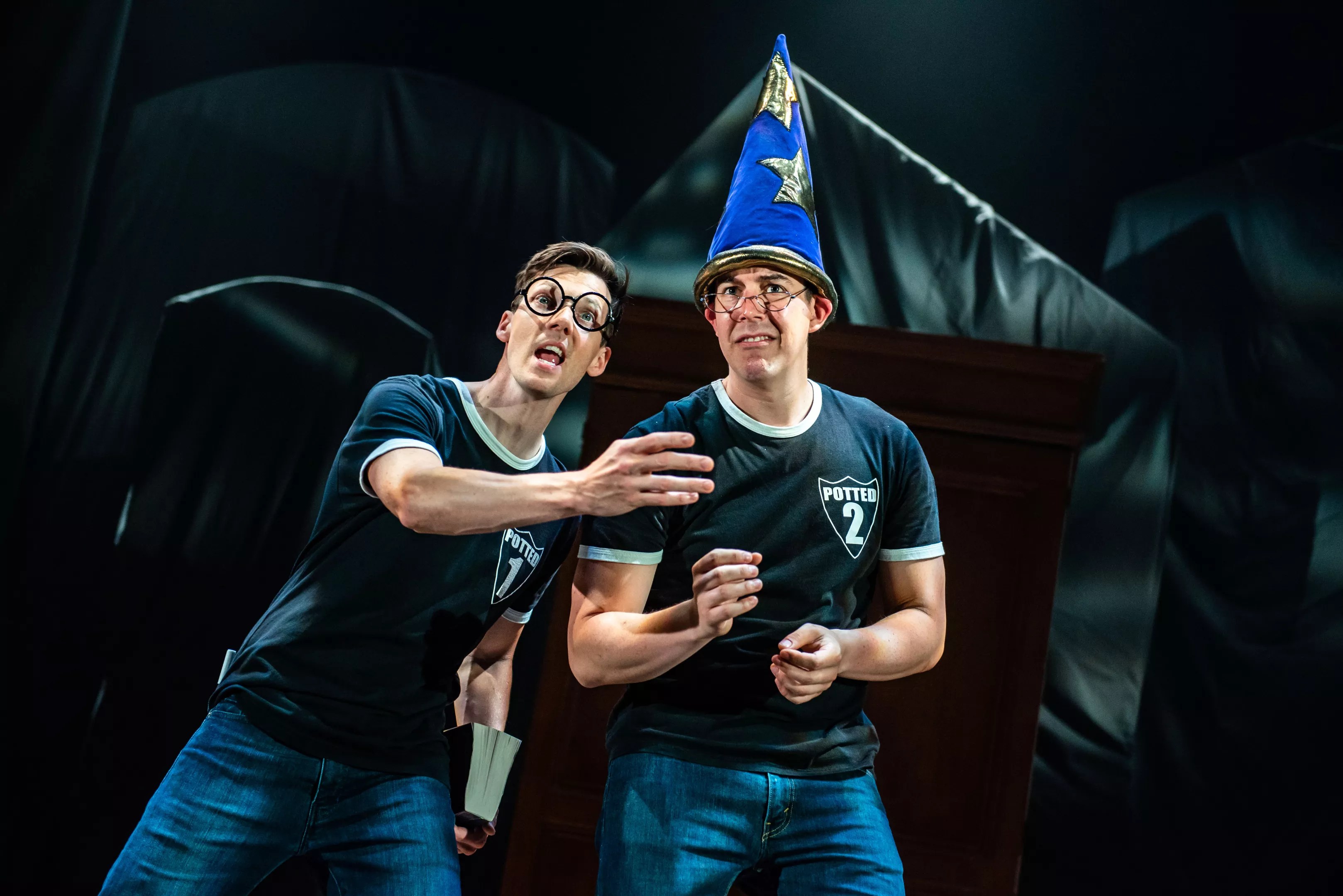 men in matching t-shirts on stage, one wearing a wizard hat