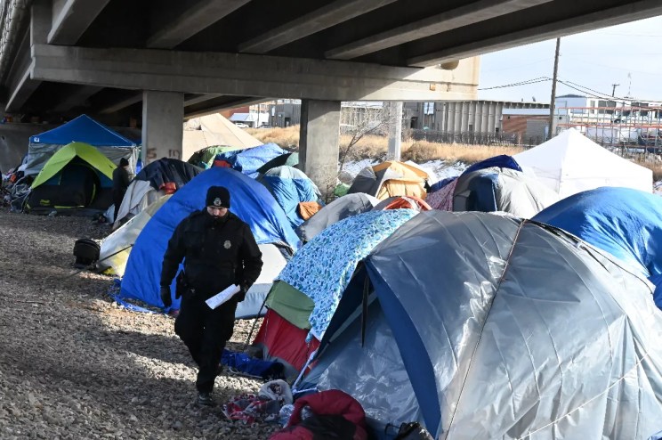 A Denver police officer walks among tents an emptied out migrant encampment.