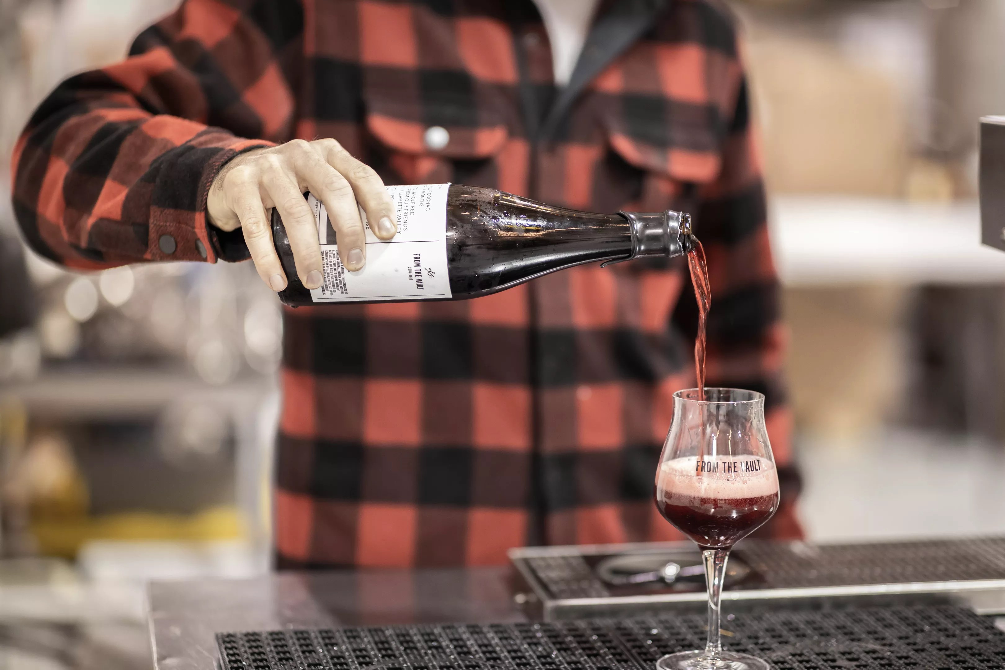 Photo of flannel shirt person pouring a beer into a glass in dramatic fashion.