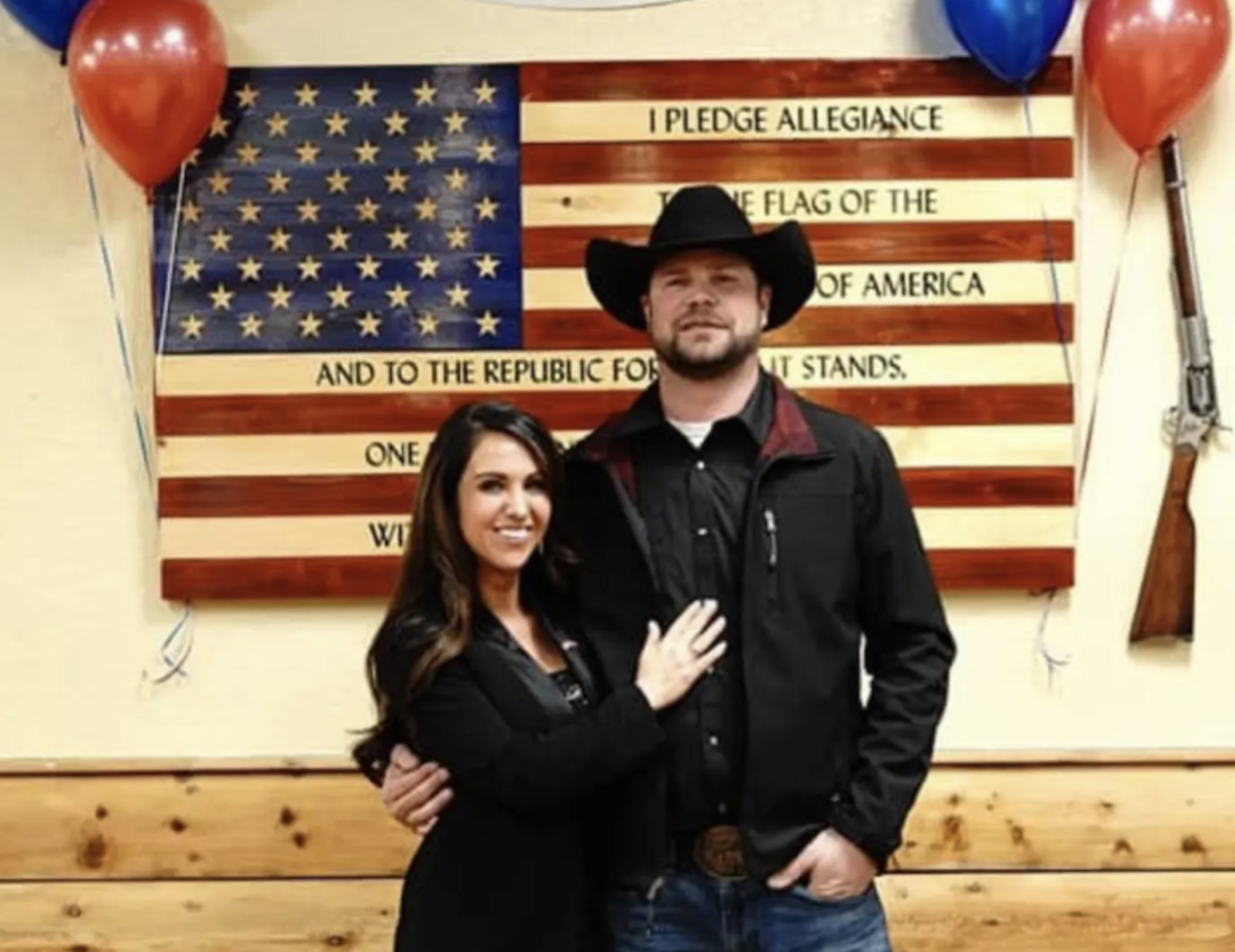 woman and man in cowboy hat in front of flag.