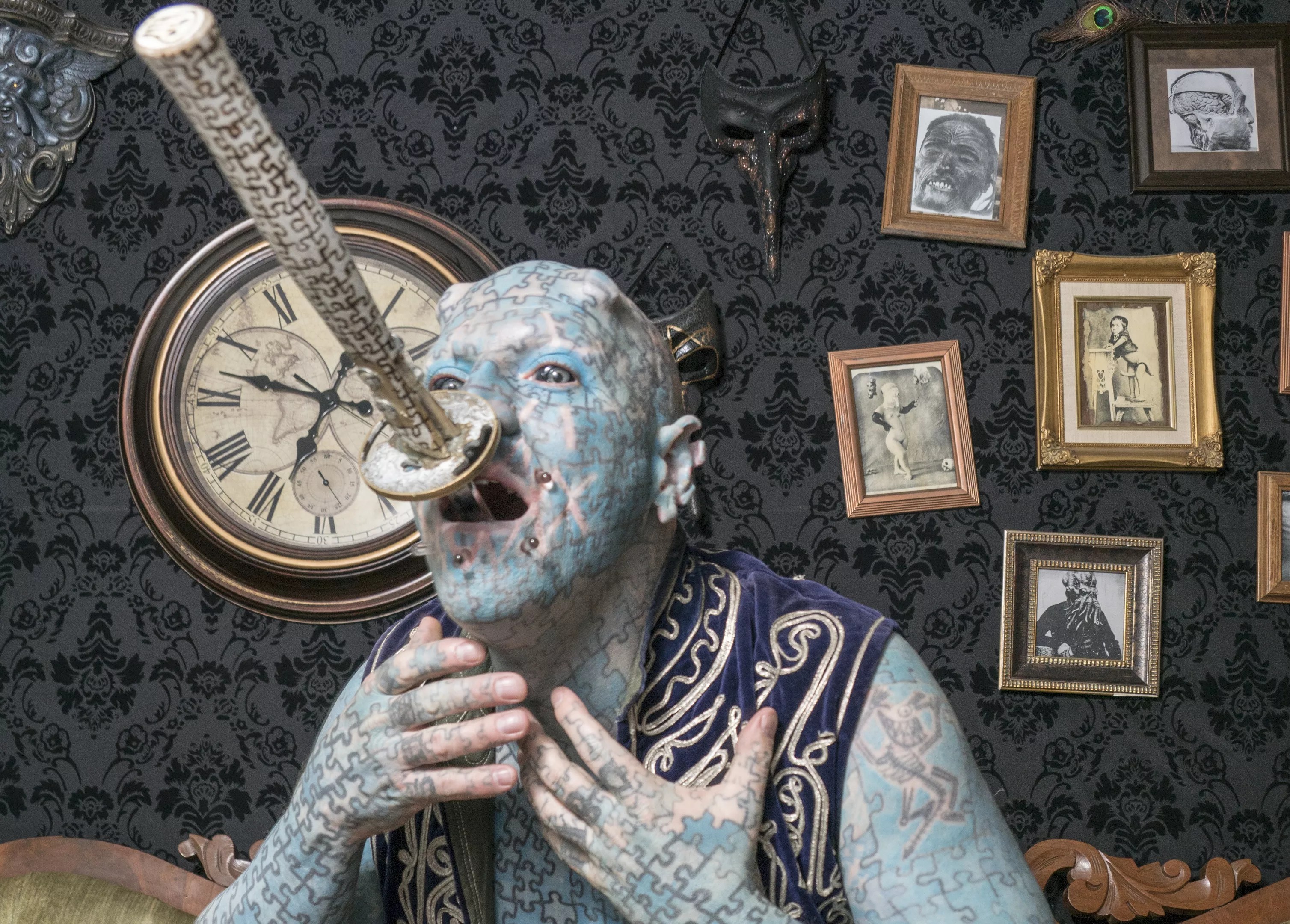man covered in blue puzzle piece tattoos swallows a sword