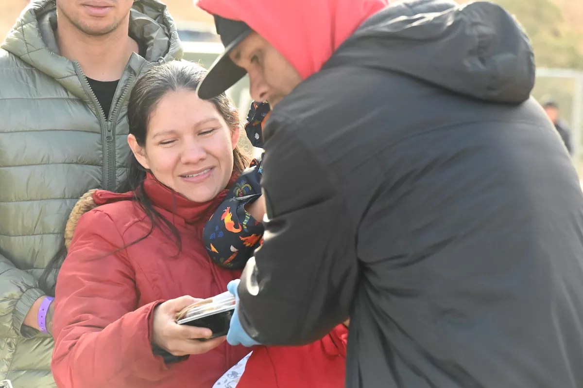 A migrant takes a packaged meal from SAME Cafe.