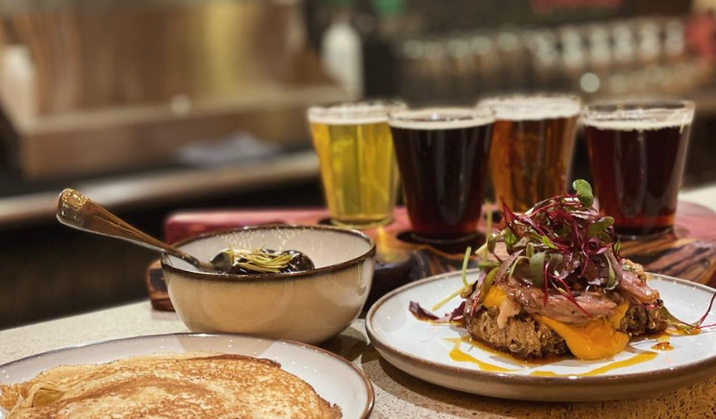 various food on plates i front of three pints of beeer