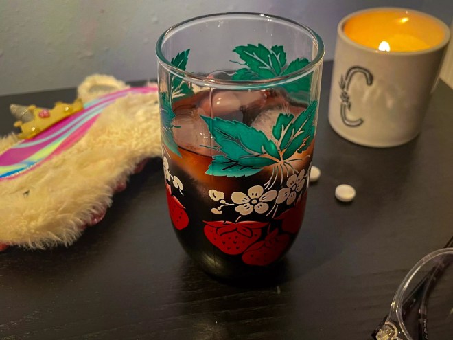 a red drink in a glass next to a candle