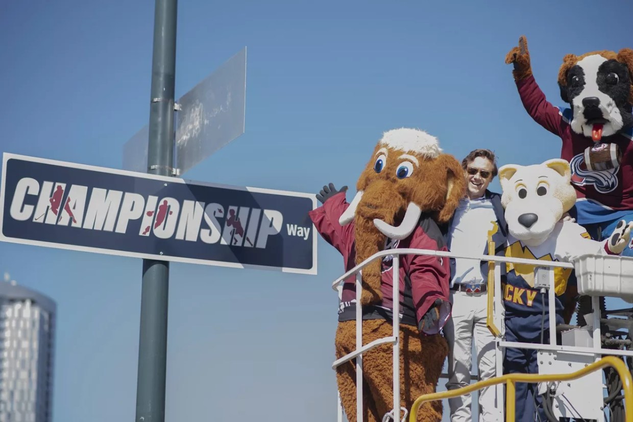 Denver mayor standing with mascots by championship sign