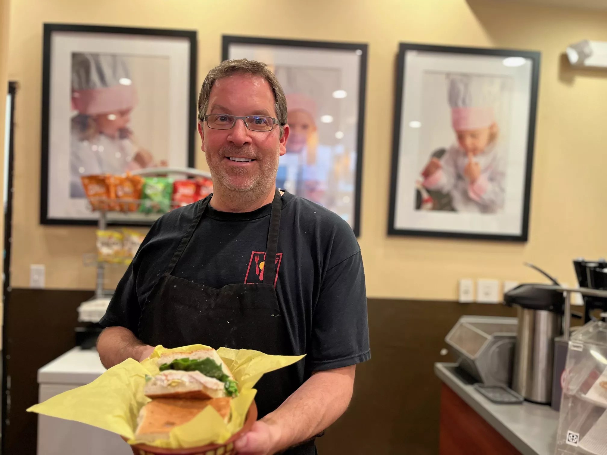 man in a black shirt holding a sandwich on a tray