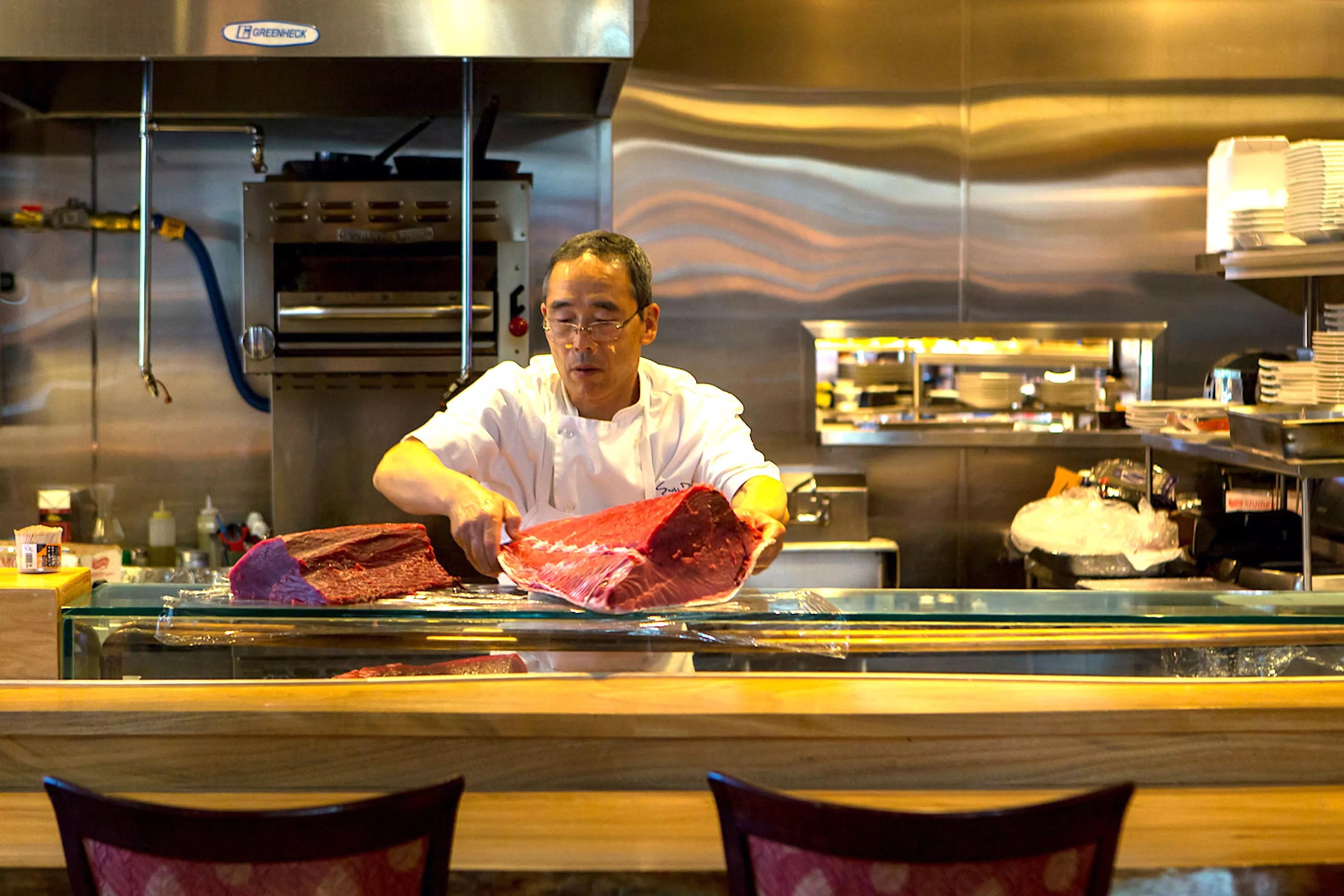 a man in a chef's coat holding a large piece of raw tuna