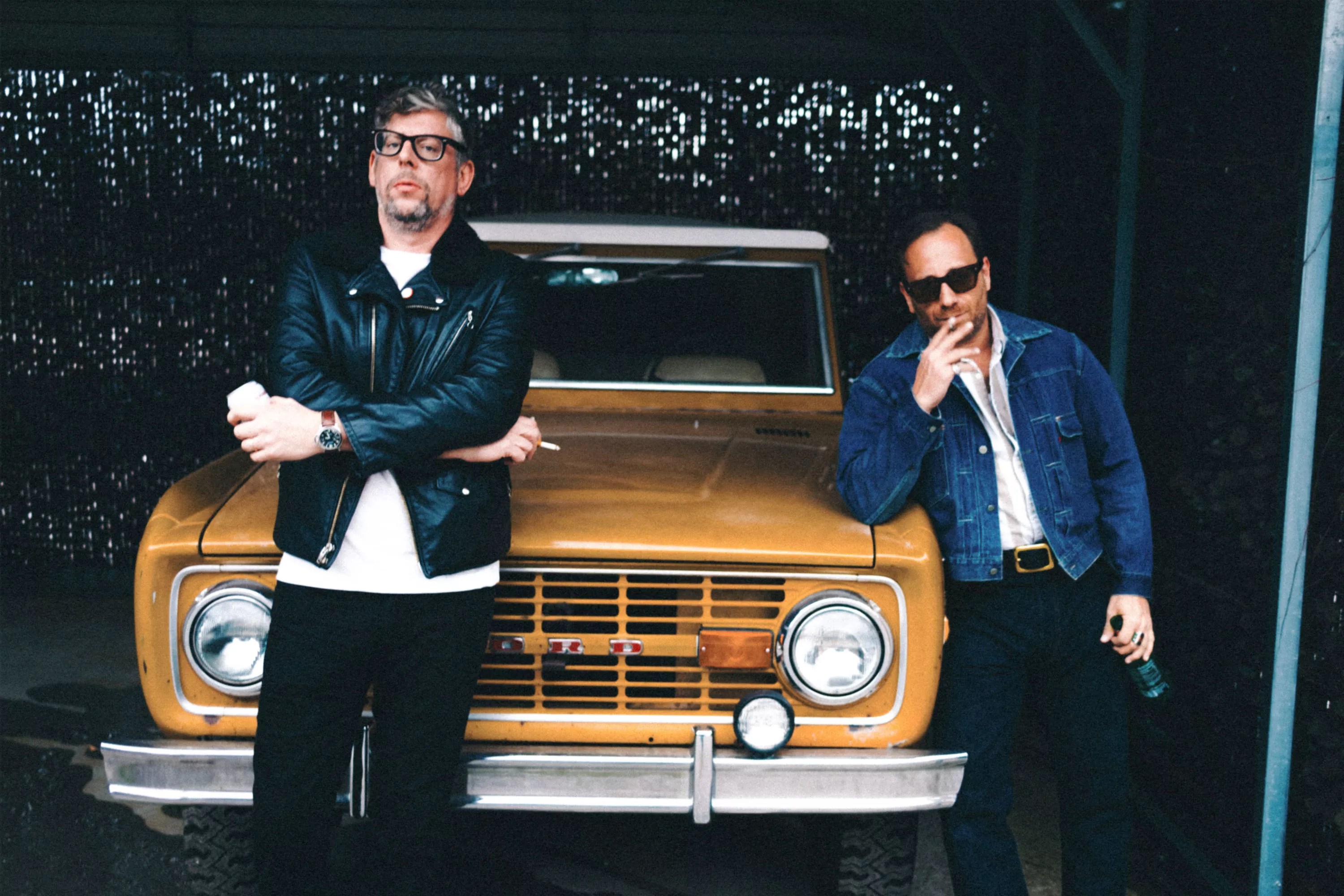 two men leaning on a yellow car