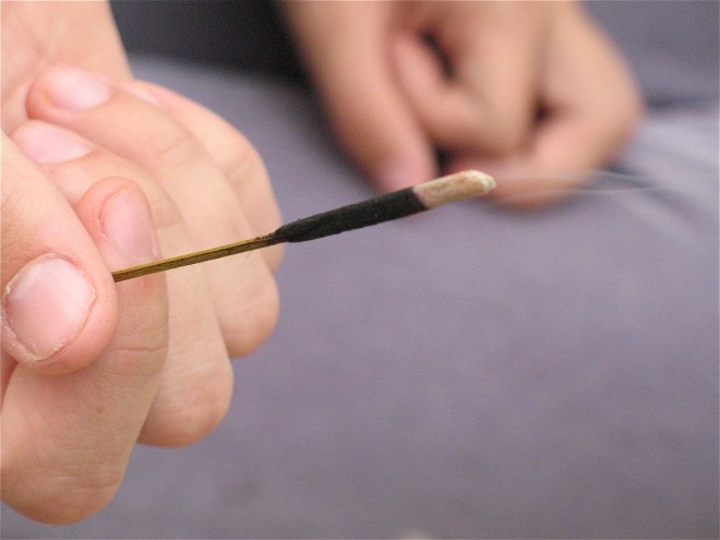 Hand holds a burning incense stick