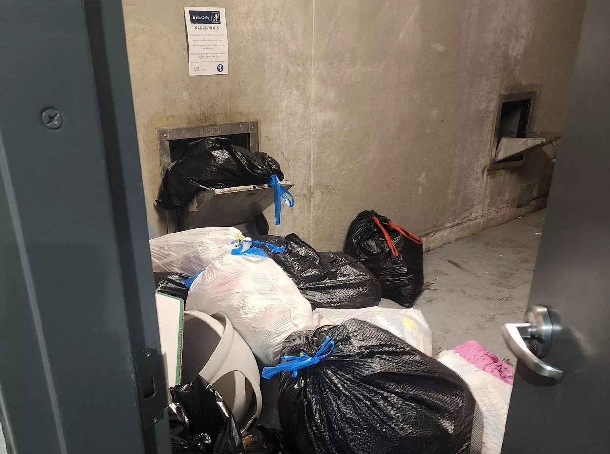 Trash bags overflow out of a garbage chute