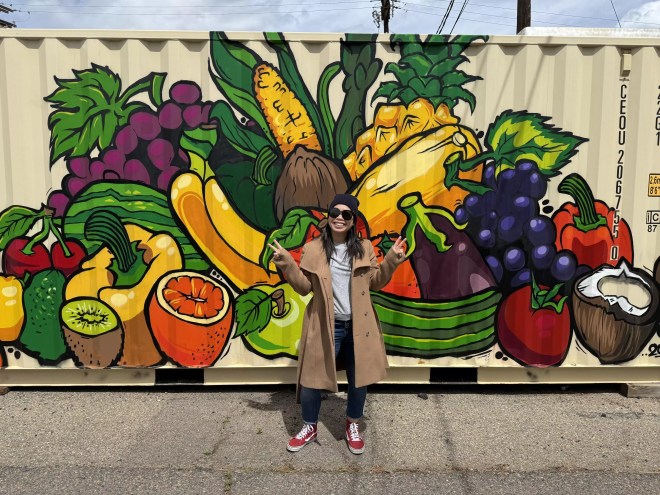 woman in glasses in front of mural.