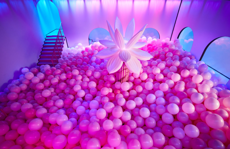 pink balloons on the floor of a room with an inflatable flower in the center