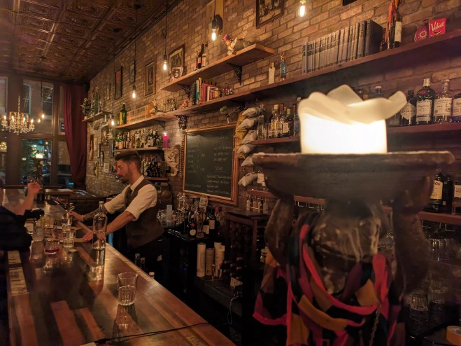 man in a vest standing behind a bar