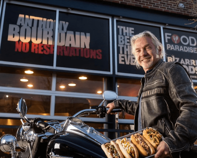 man standing next to a motorcycle holding a tray of hot dogs