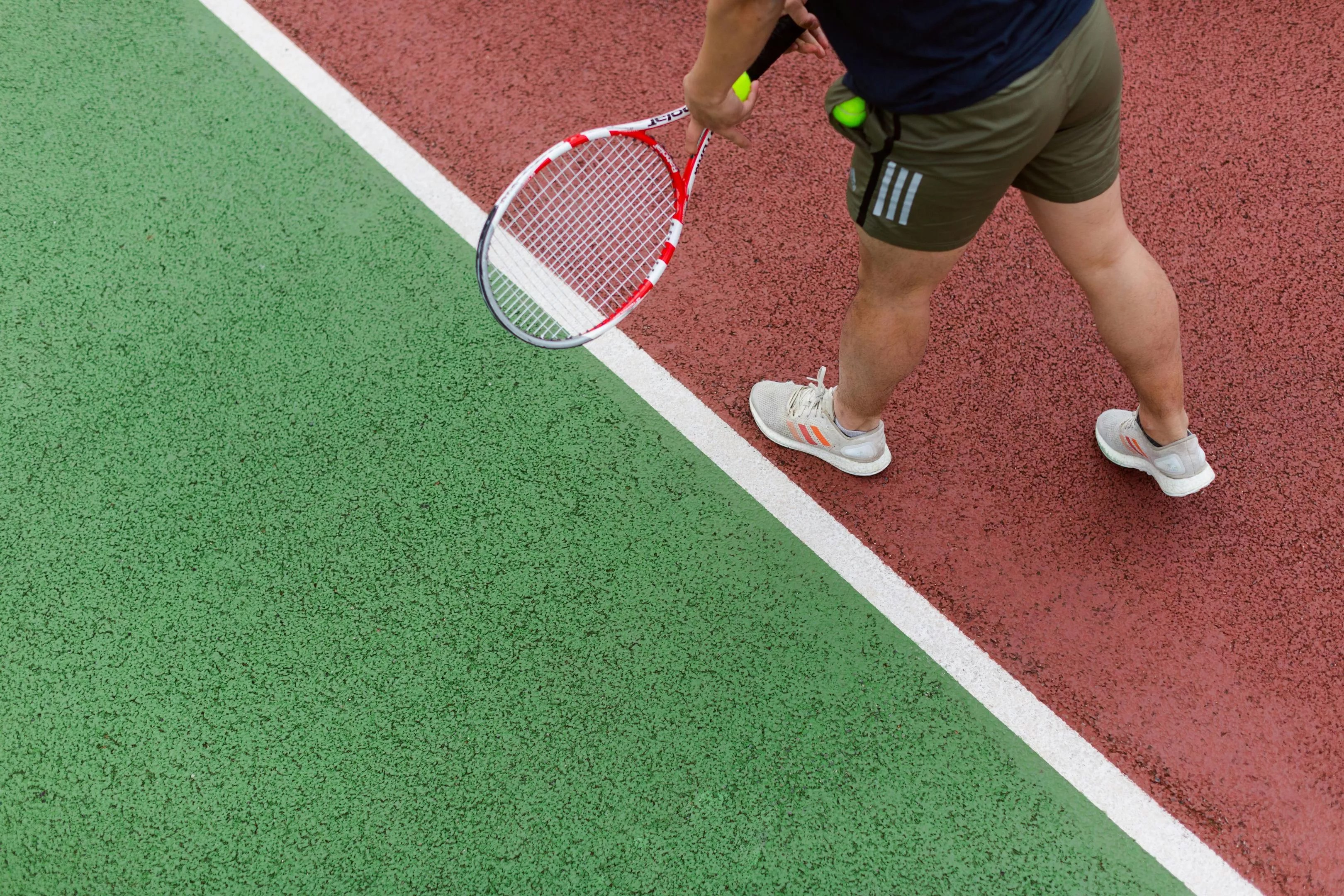 A tennis player holding a racket and a tennis ball prepares to serve.