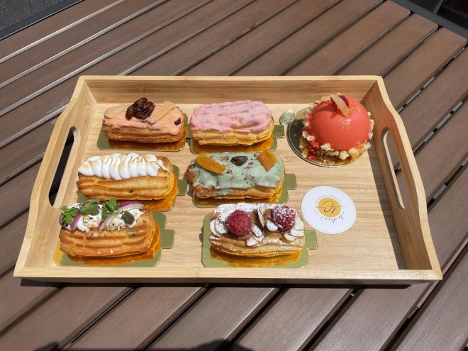a variety of colorful eclairs on a wooden tray