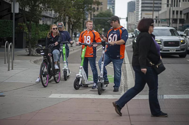 A group of four adults riding standing e-scooters in downtown Denver.
