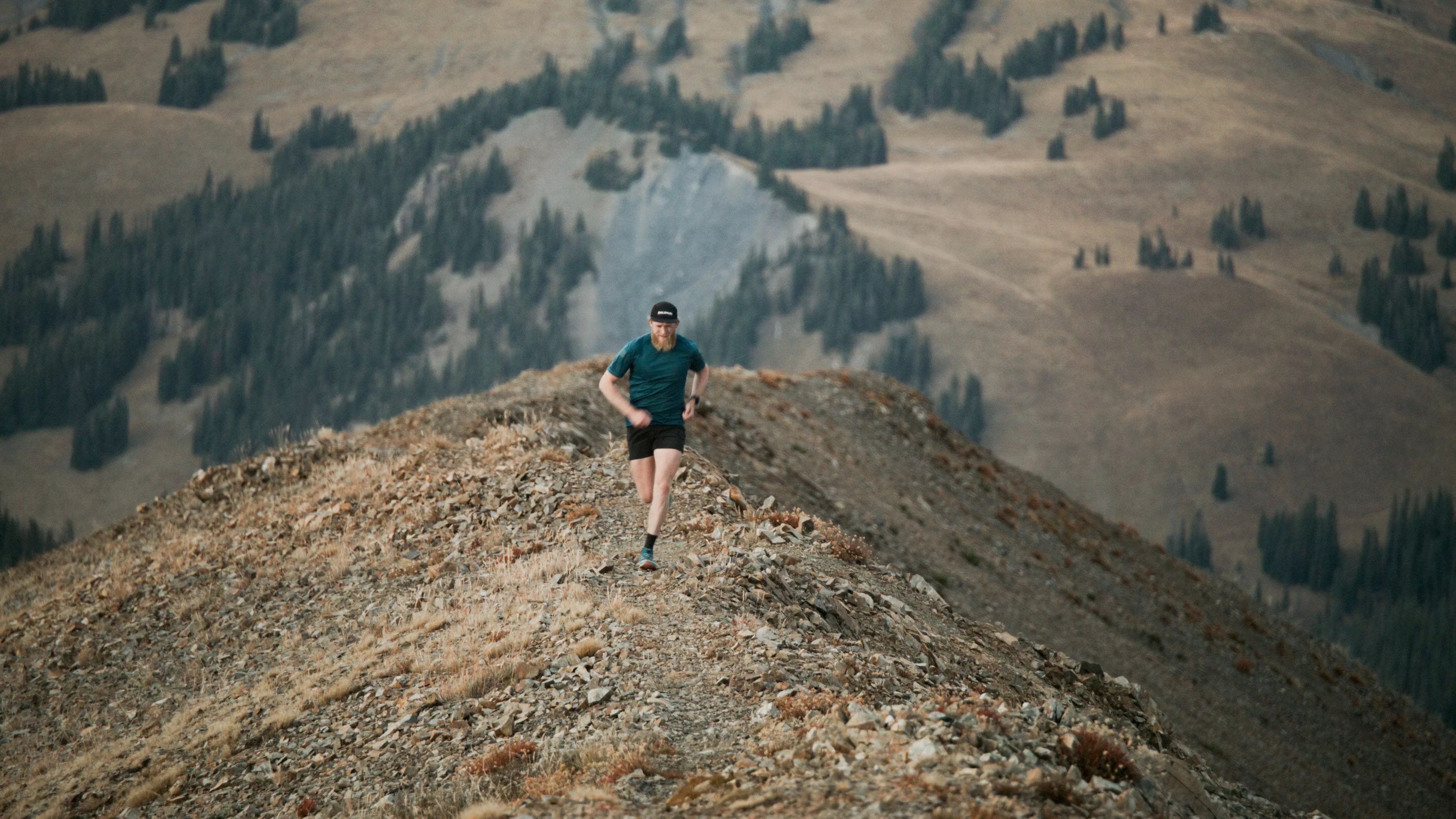 Drew Petersen wearing a blue shirt and black shorts while running up a rocky trail