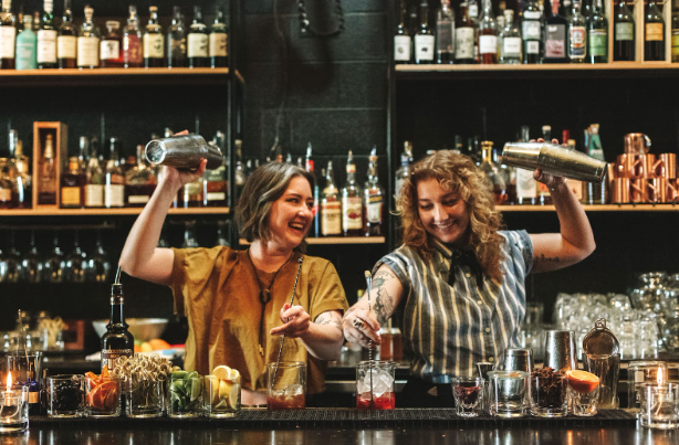 two women shaking drinks behind a bar