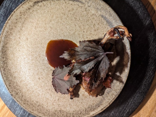 leg of squab on a plate under dark purple leaves