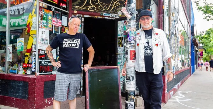 Two men stand in front of store and chalkboard