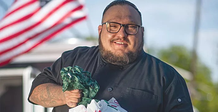 man in front of flag with green chiles