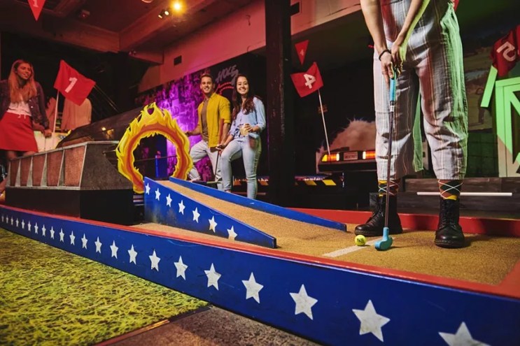 Three players watching another line up a shot at Holey Moley Golf Club