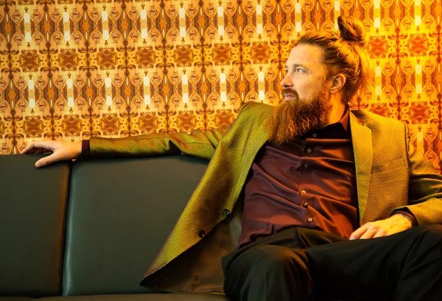 Man with pony tail sits on couch