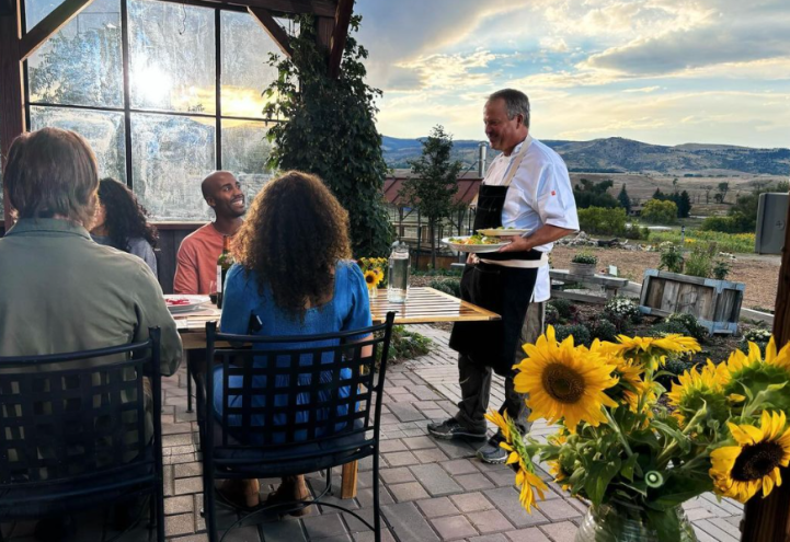 man in a apron serving food to guests at a table