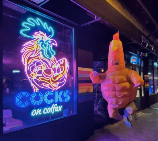 person in a chicken suit next to a neon sign