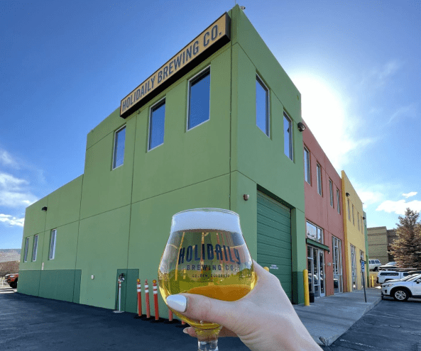 Green brewery building in background, beer in foreground.