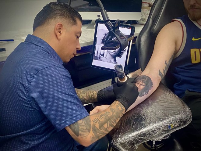 A shot of Artis Garcia tattooing a portrait of Jim Morrison on the inner forearm of a client.