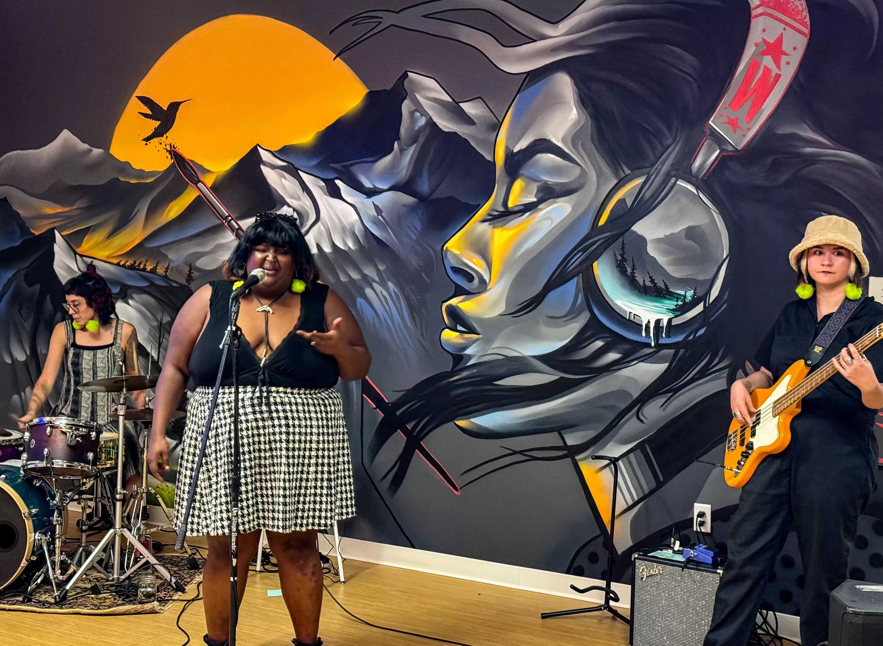 a drummer, singer and bassist performing in front of a mural