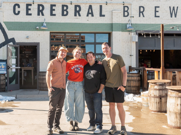 four people posing for a photo in front of a brewery