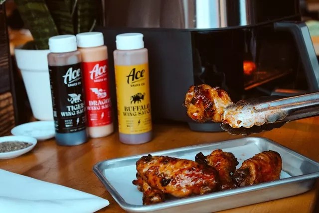 three sauce bottles behind a tray of chicken wings
